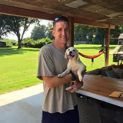 A man standing on a patio holding a yellow Labrador puppy.