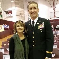 A woman standing next to a man in a U.S. Army dress uniform in a gymnasium.